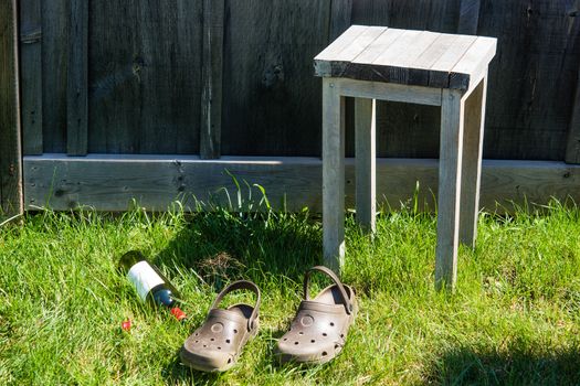 Two old shoes, a stool and an empty bottle of wine on the grass near the fence