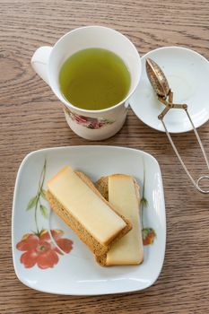 Green tea in a cup and two rusks with a hard yellow cheese on a saucer