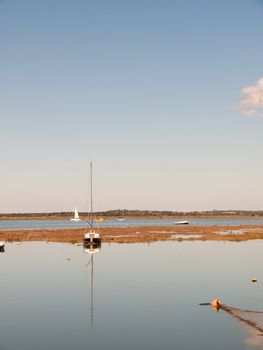 boat moored in estuary scene with mast reflected in water blue sky; essex; england; UK