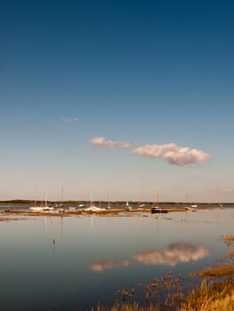 beautiful estuary scene with blue sky moored boats, masts, and reflection of cloud in water surface; essex; england; UK