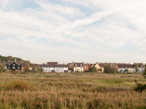 row of houses on coast edge behind field across the way sky and grass; Essex; England; UK