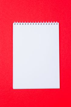 Top view of open spiral blank notebook on red paper background
