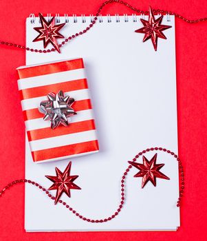 Holiday decorations and notebook and gift on red background