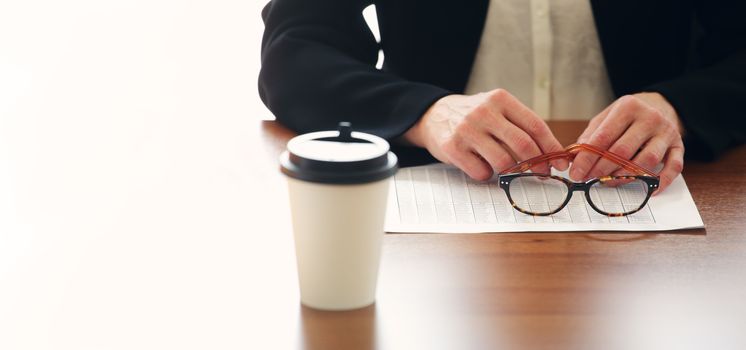 Closeup view of businessman sitting at office table with takeaway coffe, chart documents and holding glasses