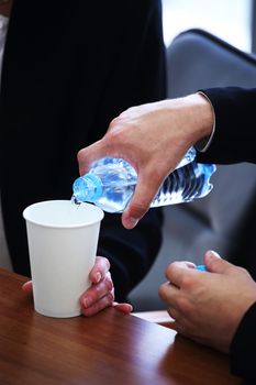 Businessman in a suit pouring water from a bottle into paper cup at business meeting