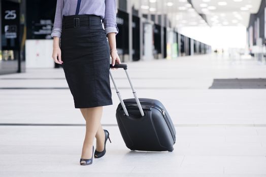 Business woman in formal clothing walking with wheeled bag at airport terminal