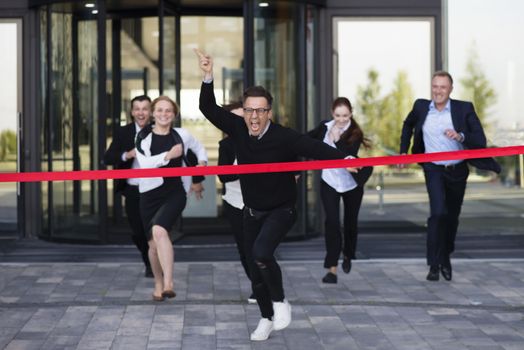 Group of happy business people running from office building crossing red ribbon finish line