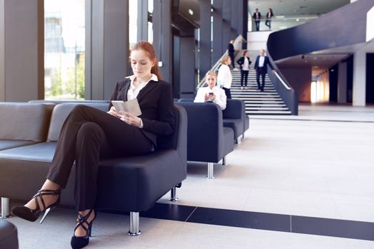 Young businesswoman sitting in lobby and surfing the net with mobile phone