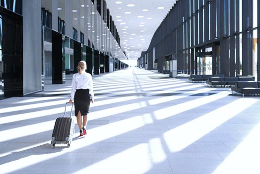 Business woman in formal clothing walking with wheeled bag at airport terminal