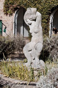 Large woman monument in park near green plants and stones. Richmond, London