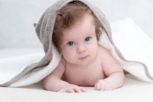 Cute newborn baby girl with beautiful blue eyes on a white terry coverlet. Adorable baby looking out under a white blanket or towel. Happy baby infant in towel after bathing in living room.