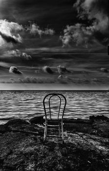 Old iron chair on the sea in black and white with dramatic clouds
