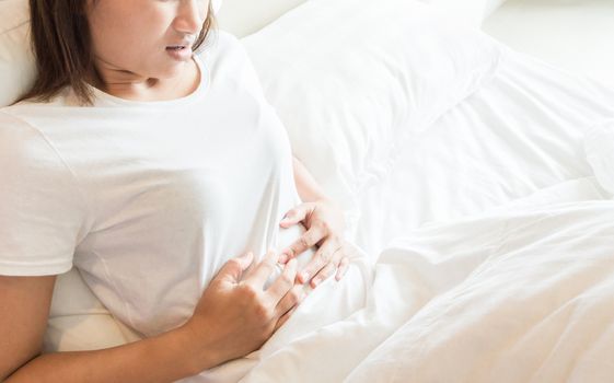 Closeup woman hand holding abdominal with stomach ache lying on bed, health care and medical concept