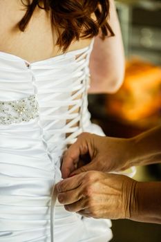 Mom is lacing up the back of her daughter's classy wedding dress.