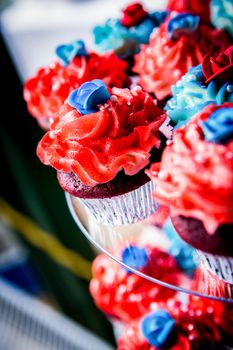 A collection of red and blue frosted cupcakes set out to eat.