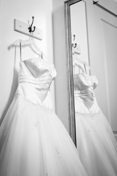 A close up of a classic wedding dress hanging up next to a mirror. 