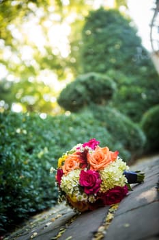 Beautiful orange, red, and yellow bouquet loaded with daisies and roses on the ground with shallow depth of field.