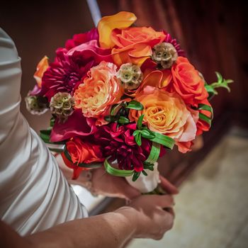 Orange, purple, green, red, bouquet being held by bride.