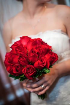 Bride holding beautiful and full red rose bouquet.