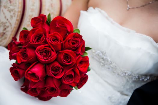 Bride holding beautiful and full red rose bouquet.