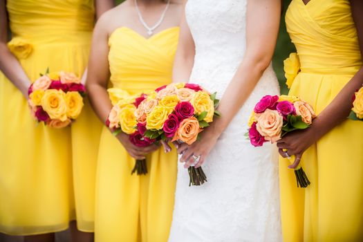 Beautiful bride holding red, yellow, orange bouquet with bridesmaids in the background.