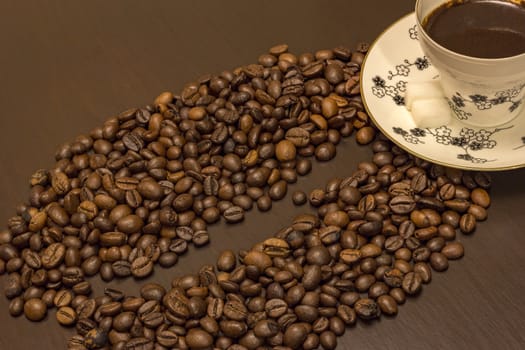 Morning coffee. A cup of coffee and coffee beans like one big bean on the table.