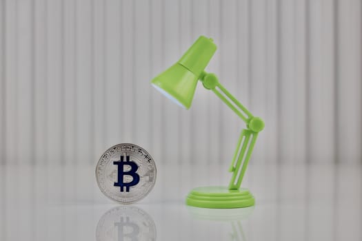 Digital currency physical blue bitcoin coin near green lamp.