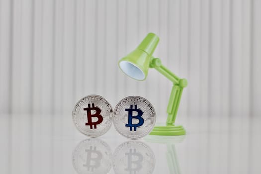 Digital currency physical silver bitcoin coin near green lamp on white table.
