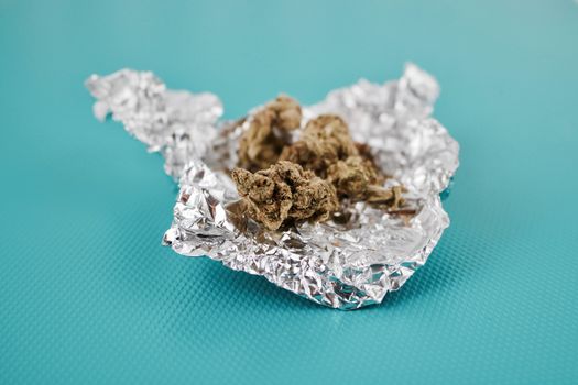 Green dry fresh marijuana in silver package on the green background.