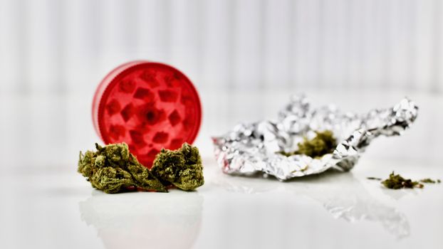 Dry green marijuana on the table, near red grinder and weed silver package.