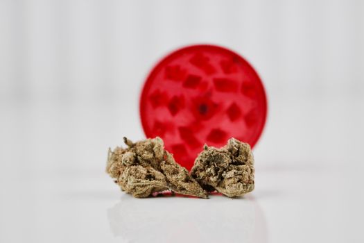 Fresh green dry marijuana plant and red weed grinder on white table.