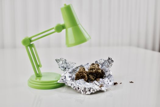 Green lamp over the dry marijuana on the white table.