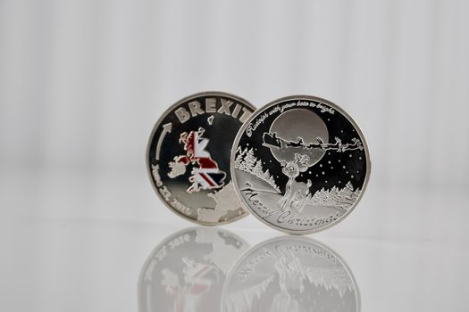 Silver brexit coin near silver christmas coin on the white table.
