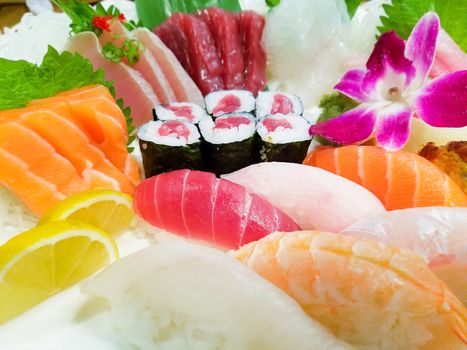 Close-up of various sushi, served on a plate with an orchid flower.