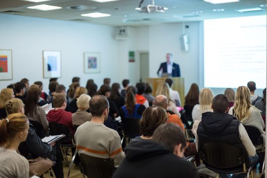 Male speaker giving presentation in lecture hall at university workshop. Audience in conference hall. Rear view of unrecognized participant in audience. Scientific conference event.