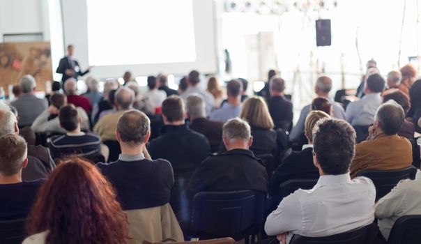 Speaker giving a talk in conference hall at business event. Audience at the conference hall. Business and Entrepreneurship concept. Focus on unrecognizable man in the audience.