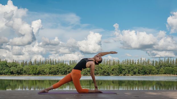 Asian woman practicing yoga pose , exercise outdoors with view of beautiful lake - relax in nature