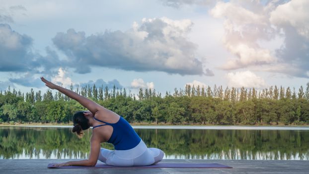Asian woman practicing yoga pose , exercise outdoors with view of beautiful lake - relax in nature
