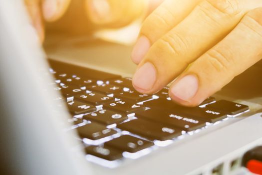 Close-up of female hands using laptop computer, working on laptop with flare light background. Searching Internet