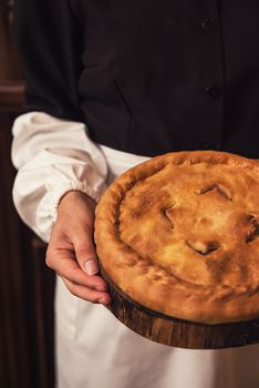 Pie from potato meat cheese and vegetables. Freshly baked pie in hands of woman in uniform