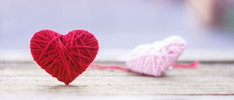 red knitting wool in shape of heart on vintage wooden with bokeh soft light background