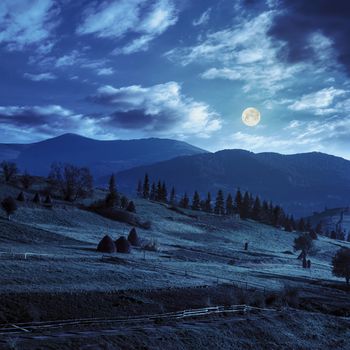 composte landscape with path near haystack  on a green meadow in the mountains at night in full moon light