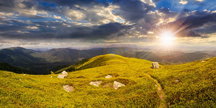 composite landscape with narrow meadow path in grass among white stones on top of mountain range in sunset light