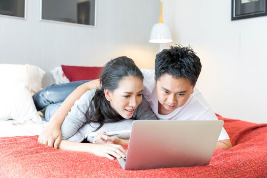 Young Asian Couples using laptop together in bedroom of contemporary house for modern lifestyle concept