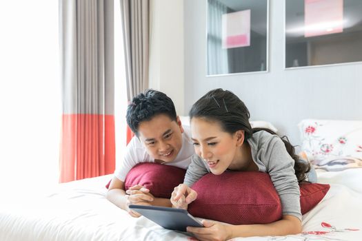 Young Asian Couples lying down and using tablet together in living room of contemporary house for modern lifestyle concept