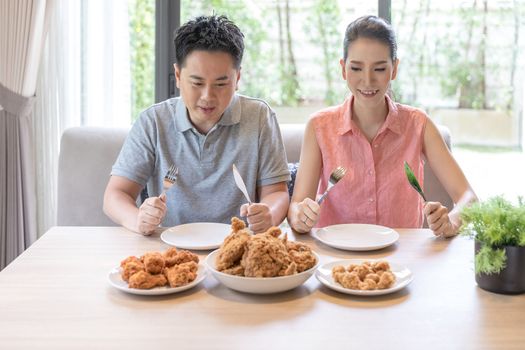 Young Asian Couples eating fried chicken together in living room of contemporary house for modern lifestyle concept
