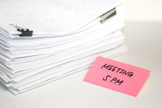 Meeting 5 PM; Stack of Documents on white desk and Background.