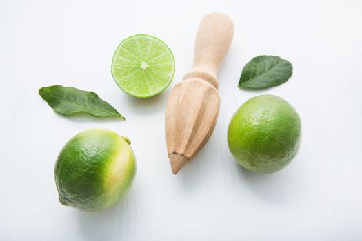 Fresh limes and wooden juicer on 
white background. Top view