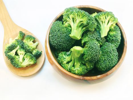 Broccoli in wooden bowl and wooden spoon on white background