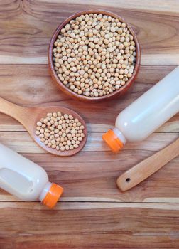 Soy milk in bottle and soy beans with wooden spoon on wooden background